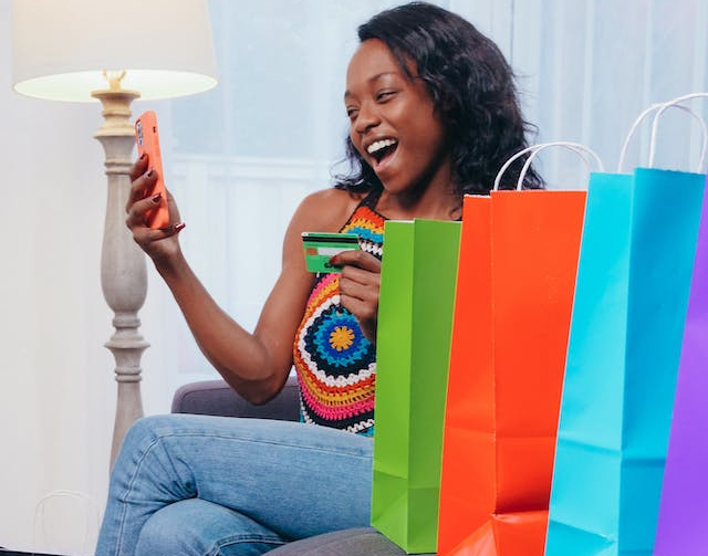 Women looking at her phone and a credit card, gifts stacked nearby
