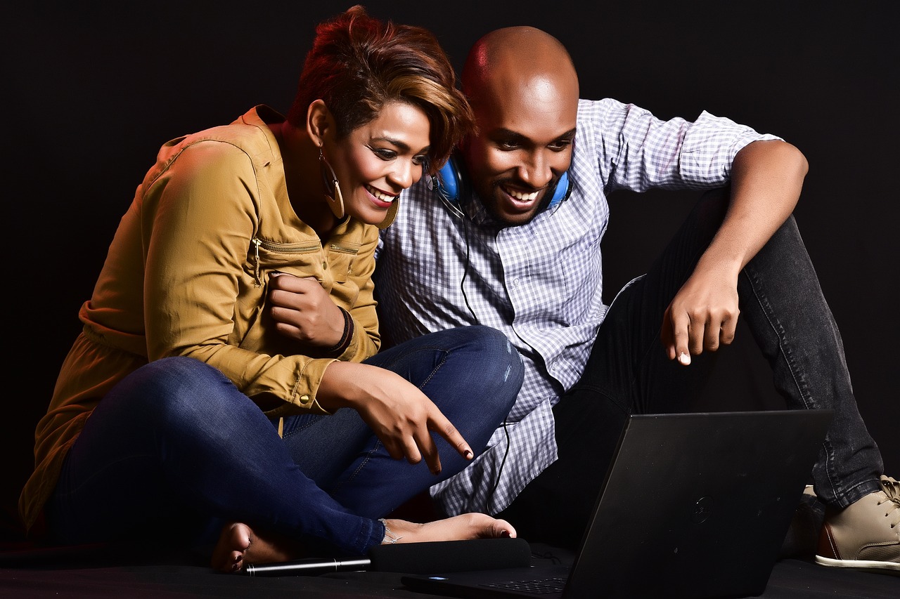 Two people sitting infront of a laptop, smiling